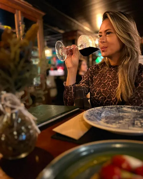 Carol em um jantar, apreciando uma taça de vinho